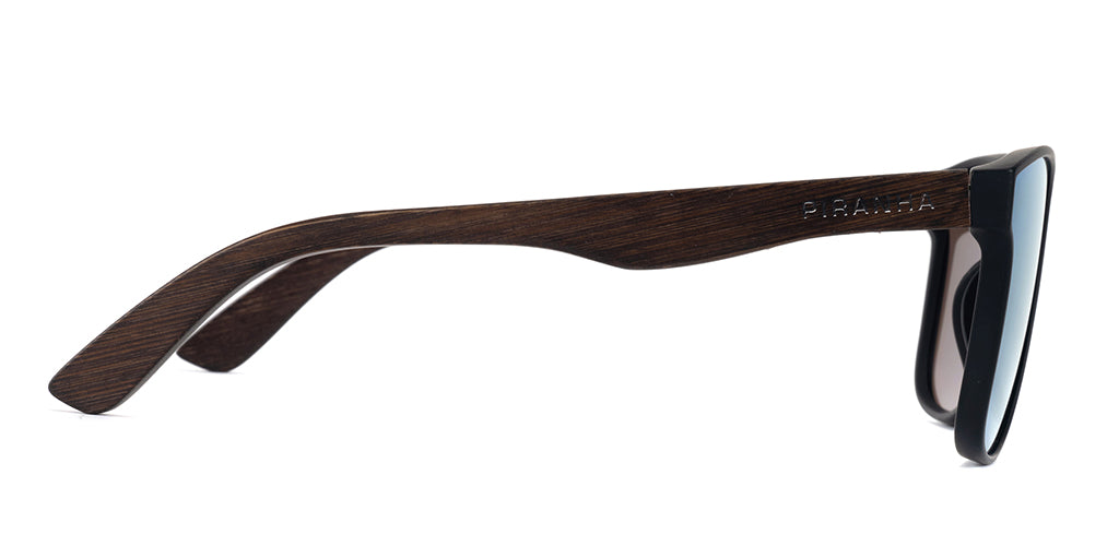 Right side facing view of a square black full rim sunglasses frame with blue mirror tinted lenses, lightweight plastic construction, dark brown bamboo temples, and a smooth finish on a white background. Featuring curved temples with san serif PIRANHA logo printed on the side.