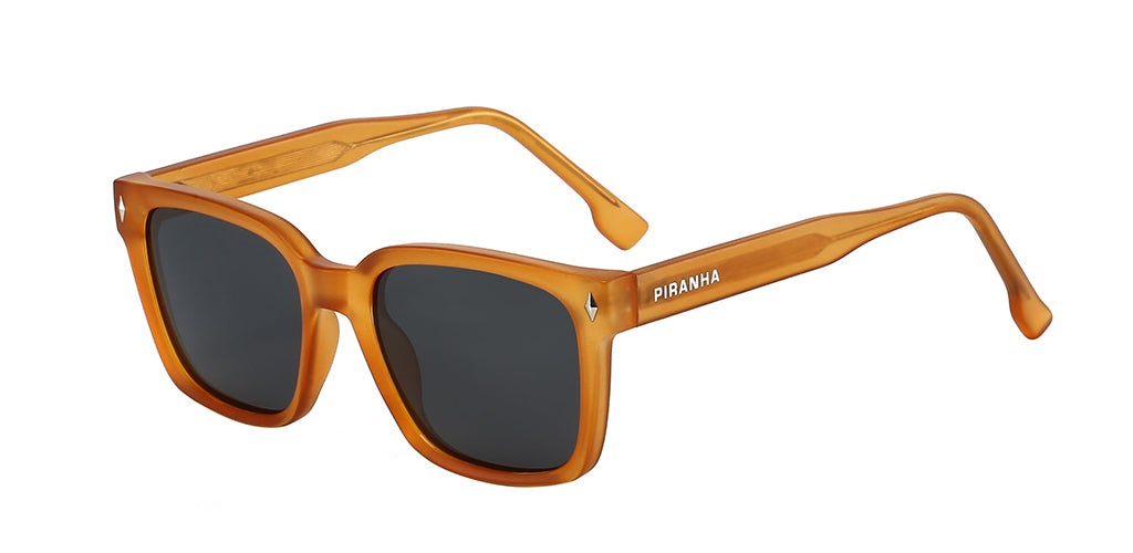 Three quarters front facing view of a vibrant orange frosted square sunglasses frame with dark gray polarized lenses. With a saddle bridge and diamond-shaped metal studs on top corners of the orange frame, which dips to meet the nose in the center. Made of plastic with a slight frosted texture - made to be lightweight and comfortable. The temples have visible metal arms embedded in frosted orange plastic - with curved eartips flaring at tip in the shape of a square. Piranha san serif logo printed on right a